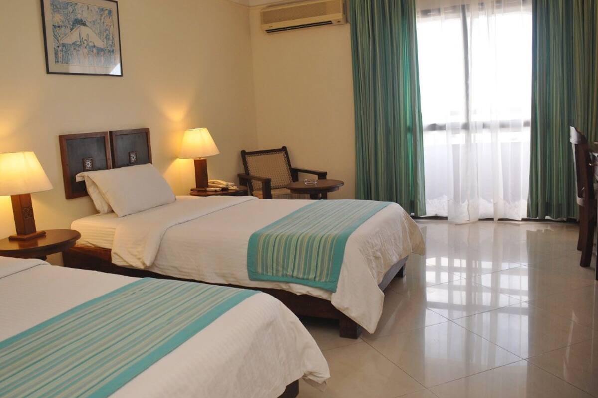 A hotel room with two beds, a chair, a table, and a painting on the wall.