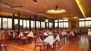 A restaurant with multiple tables and chairs, large windows, and ceiling fans. - Royal Court Hotel (Mombasa)