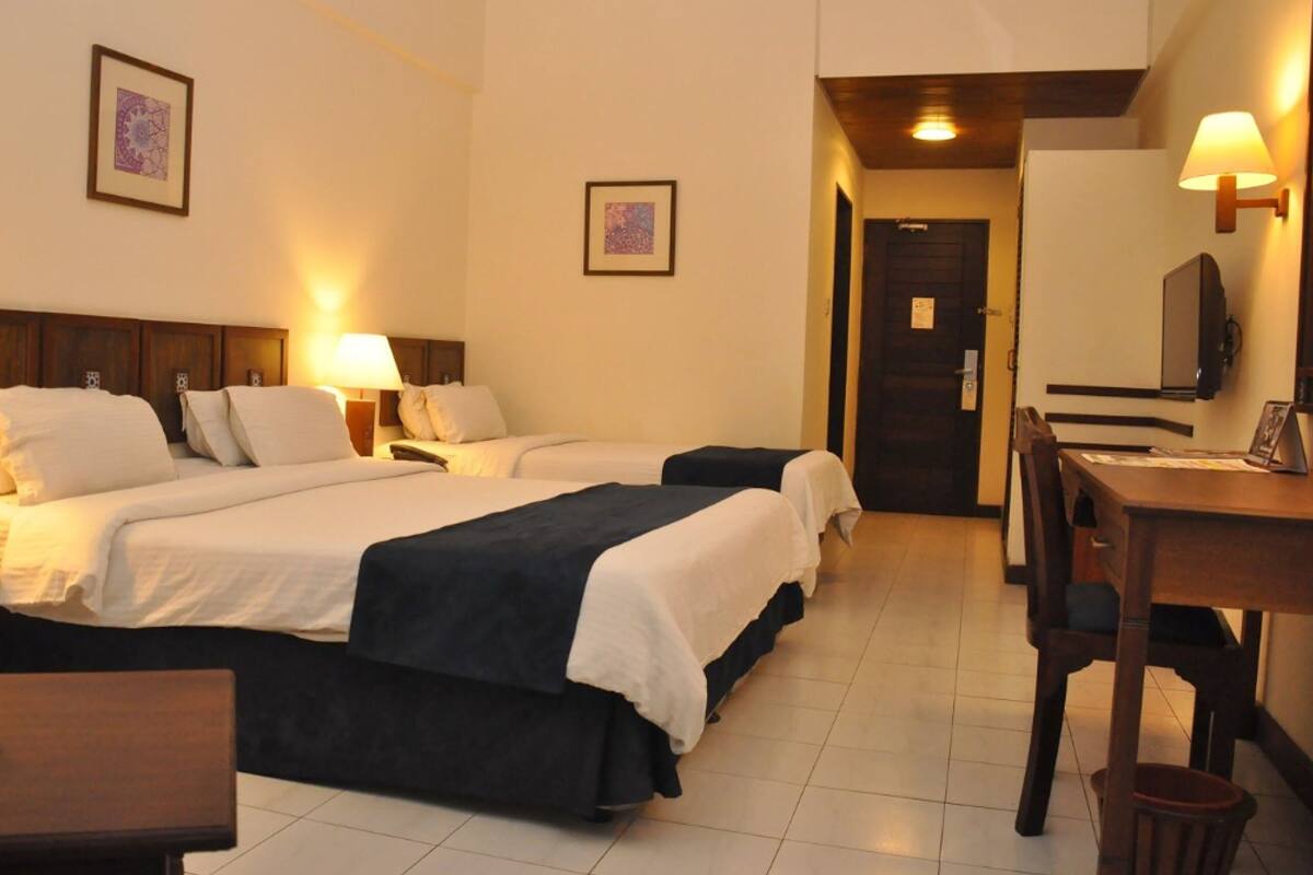 A hotel room with two beds, a desk, a chair, a TV, and two framed pictures on the wall.