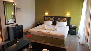 A neatly made bed with white linens, a bedside table with a vase of flowers, and a mirror on the wall. - Anna Apartments (Corfu)