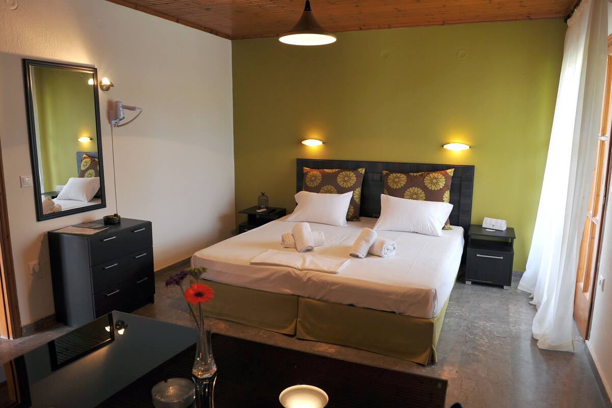 A neatly made bed with white linens, a bedside table with a vase of flowers, and a mirror on the wall.