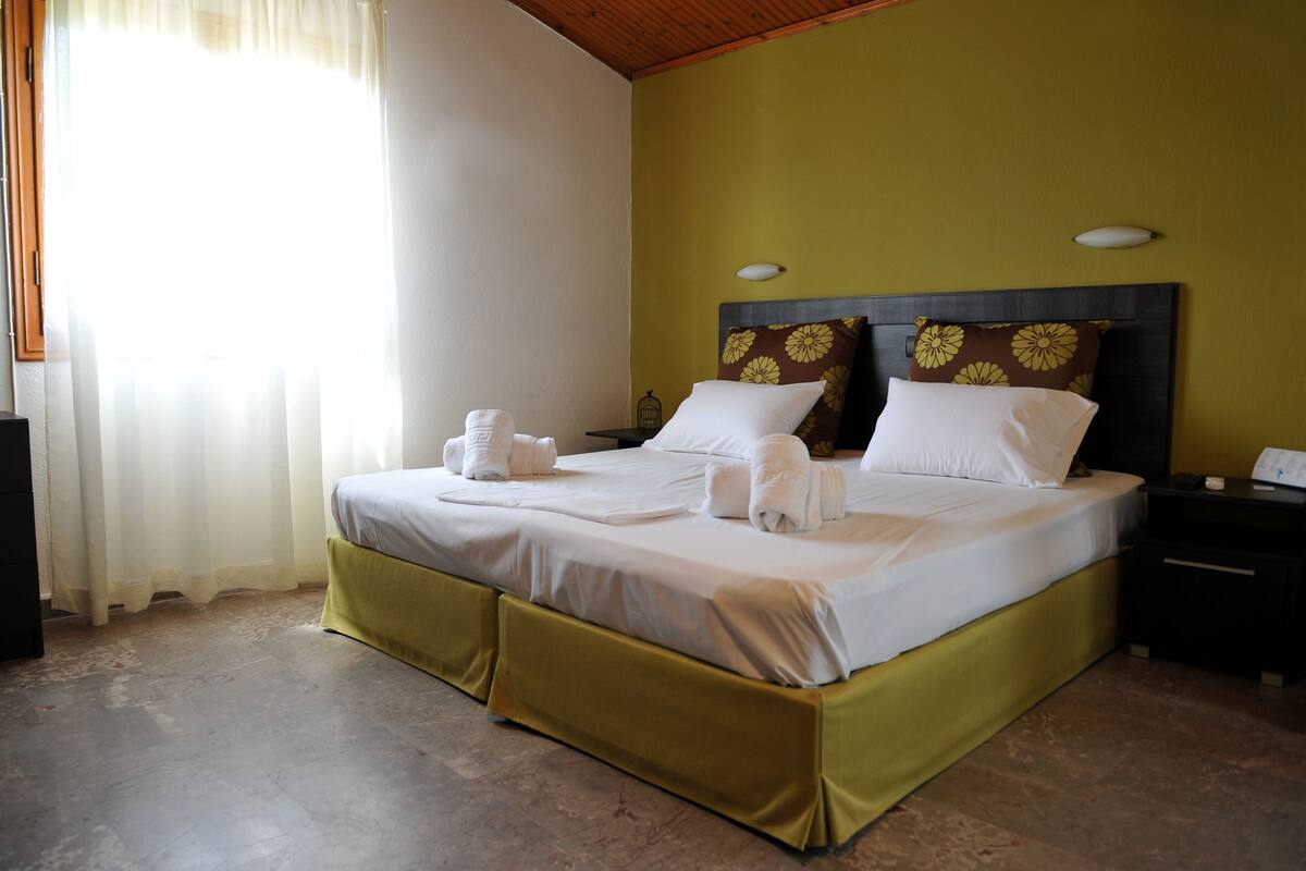 A neatly made bed with white linens and towels, a wooden headboard, and a nightstand with a lamp.