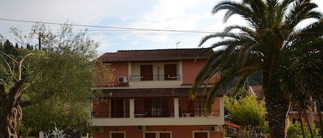A two-story building with a red facade, multiple balconies, and a gated entrance.