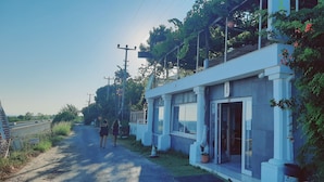 A building with a white facade, large windows, and a door. There is a pathway leading to the entrance, and a person is walking towards the building. - Dallas Hotel (Marmara Ereglisi)