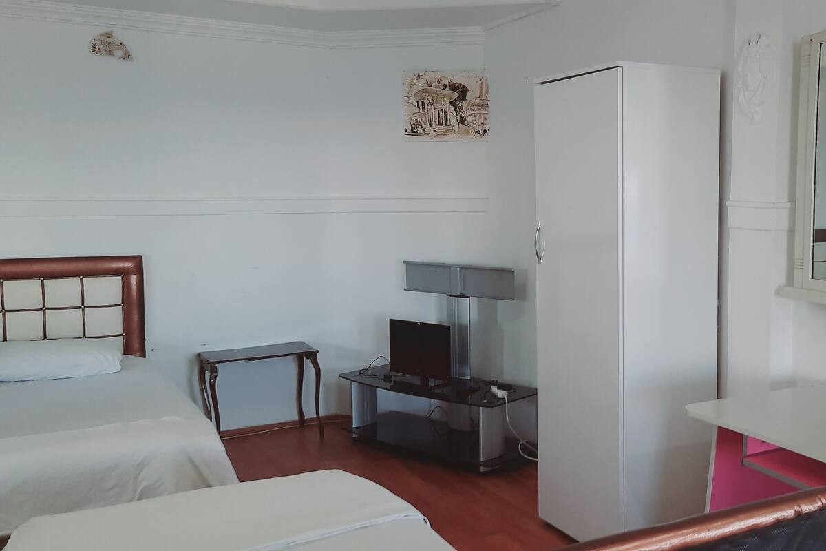 A hotel room with two beds, a desk with a computer, a refrigerator, and a mirror.
