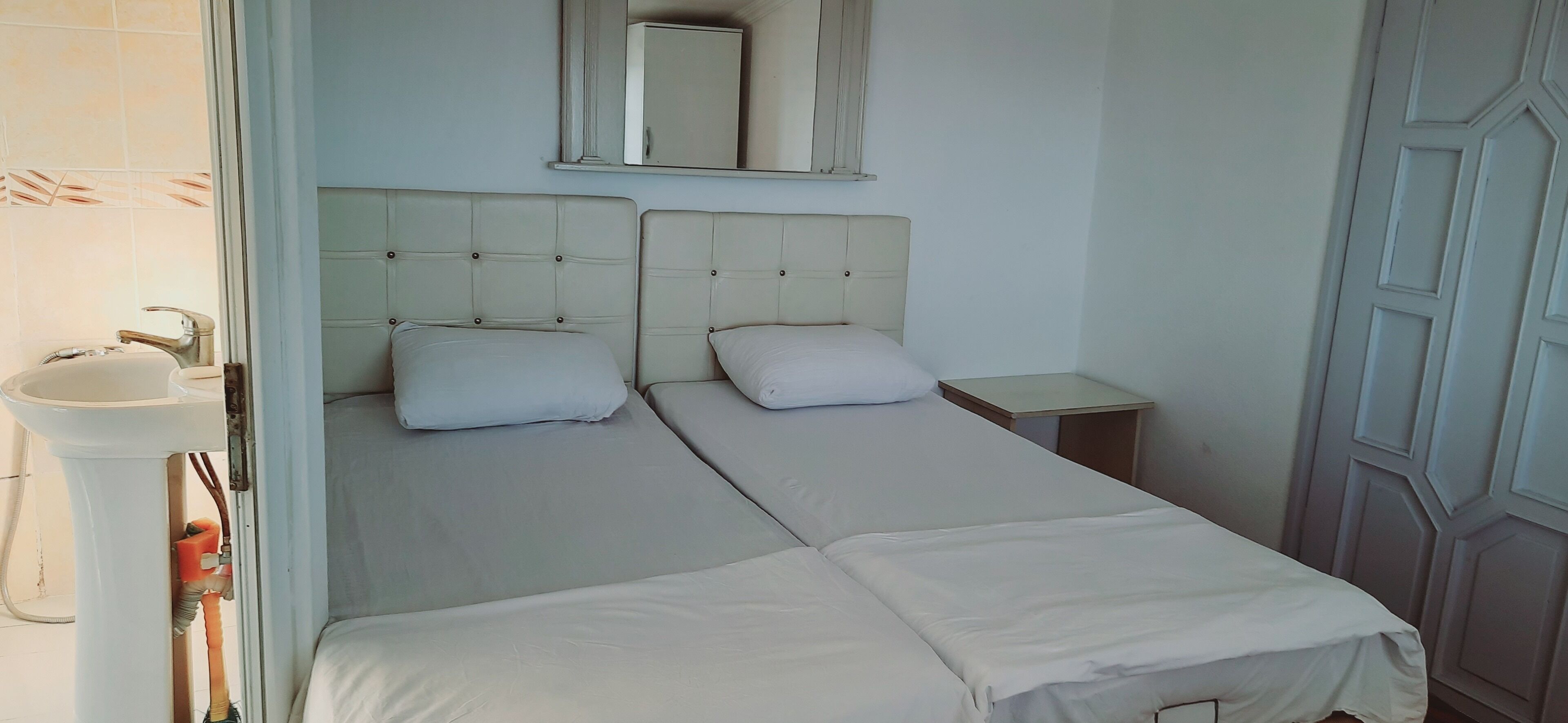 Un dormitorio con dos camas, una mesita de noche, un espejo y un lavamanos.