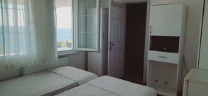 Un dormitorio con dos camas, una ventana con cortinas translúcidas, un armario blanco y vistas al mar.