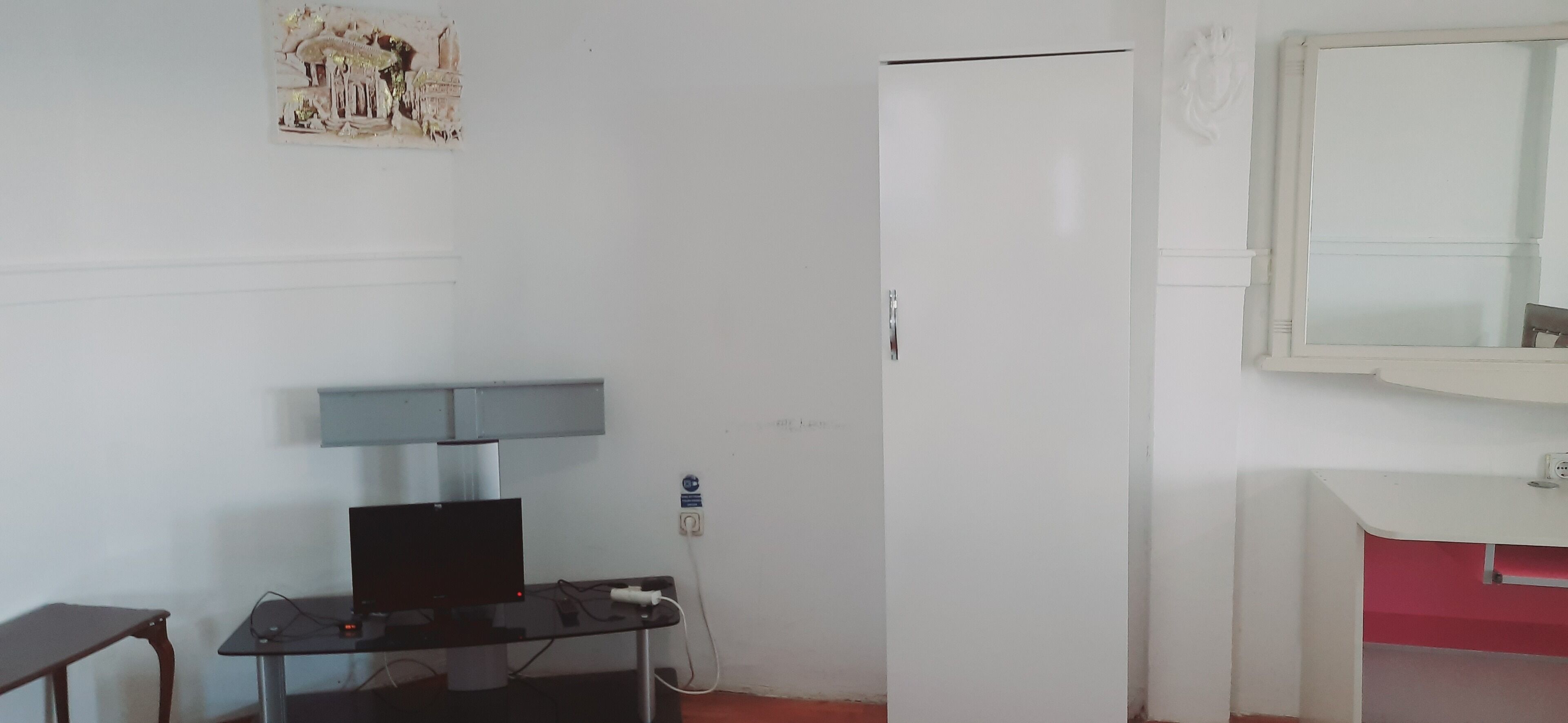 Una habitación con un escritorio, una computadora, una puerta blanca y un espejo.
