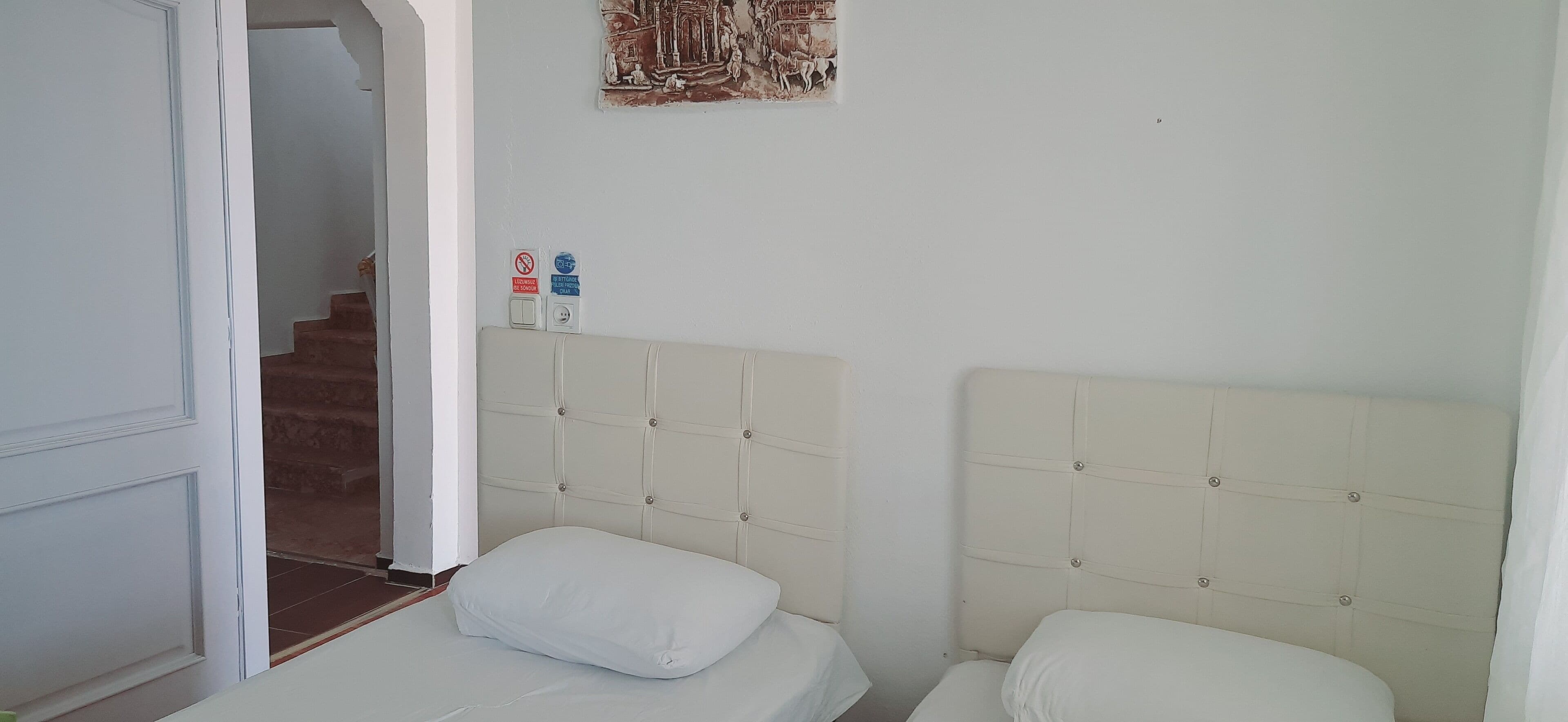 Una camera da letto con due letti, una porta che dà su una scala e un interruttore della luce fissato al muro.