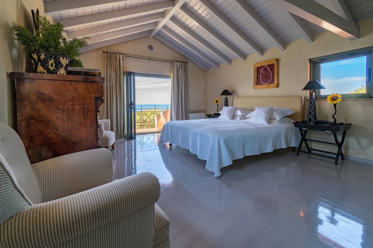 A bedroom with a bed, a nightstand, a lamp, a dresser, and a view of the outdoors.