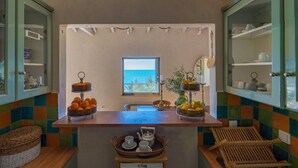 Une cuisine avec vue sur la mer, une fenêtre et un comptoir agrémenté de paniers de fruits et d’ustensiles de cuisine.