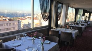 Un restaurante con mesas dispuestas para comer, amplias ventanas con cortinas y vistas a la ciudad.