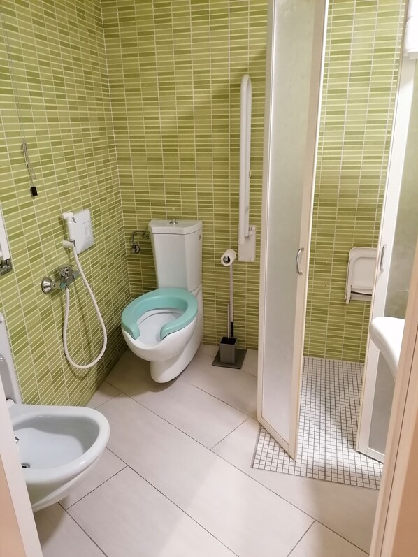 Ein Badezimmer mit Toilette, Bidet und Bidetbrille, geflieste Wände und einer Duschkabine.