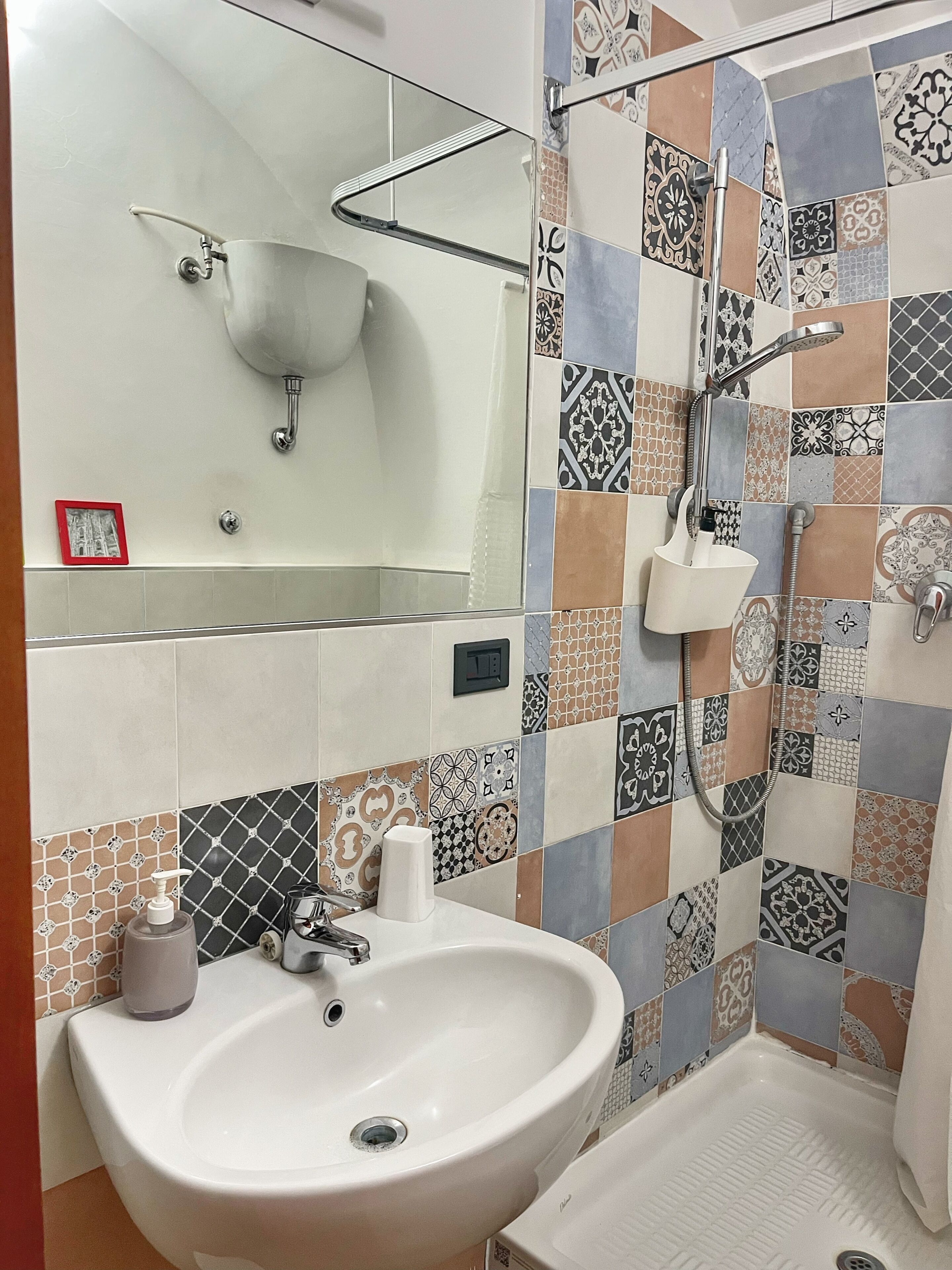 Baño con lavamanos, espejo, ducha y azulejos estampados.