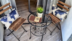 A small outdoor seating area with two wooden chairs and a round table, each with a world map pillow. A small potted plant is on the table. - Chiostro San Marco (Tarquinia)