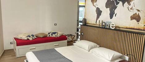 A bedroom with a bed, a red sofa, a world map on the wall, and a 'Home' sign.