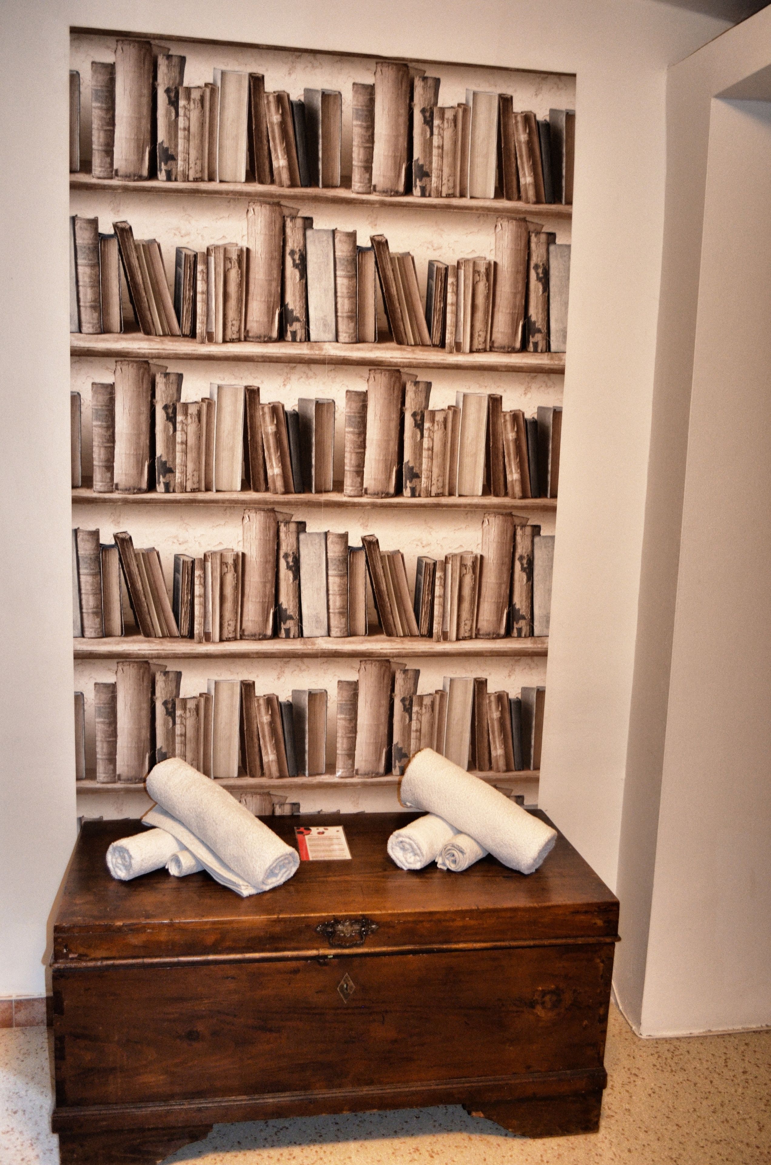 Une bibliothèque remplie de livres et deux serviettes enroulées posées sur un coffre en bois.