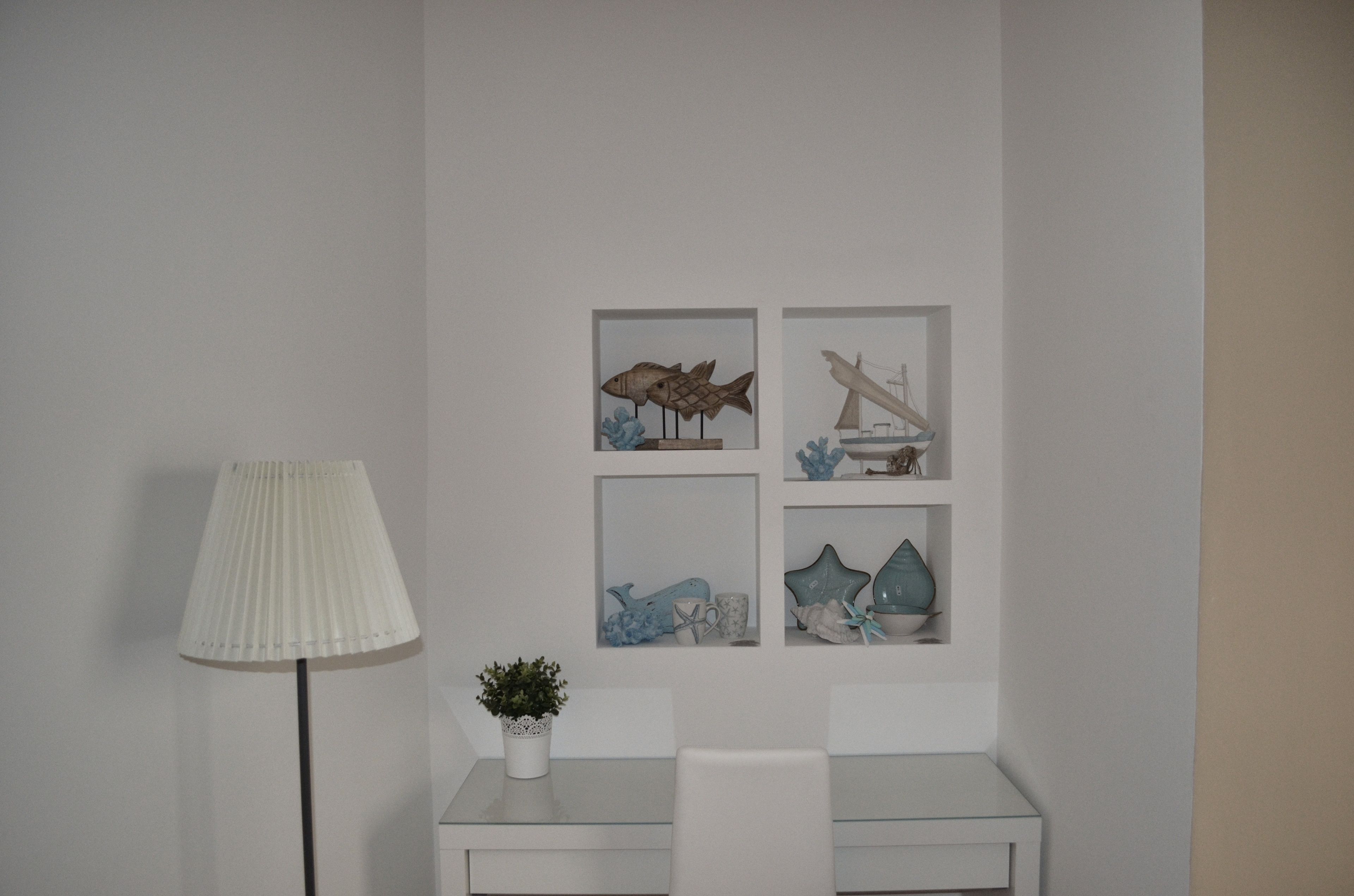 A minimalist room with a white desk, a lamp, and wall-mounted artwork depicting marine life and a ship.