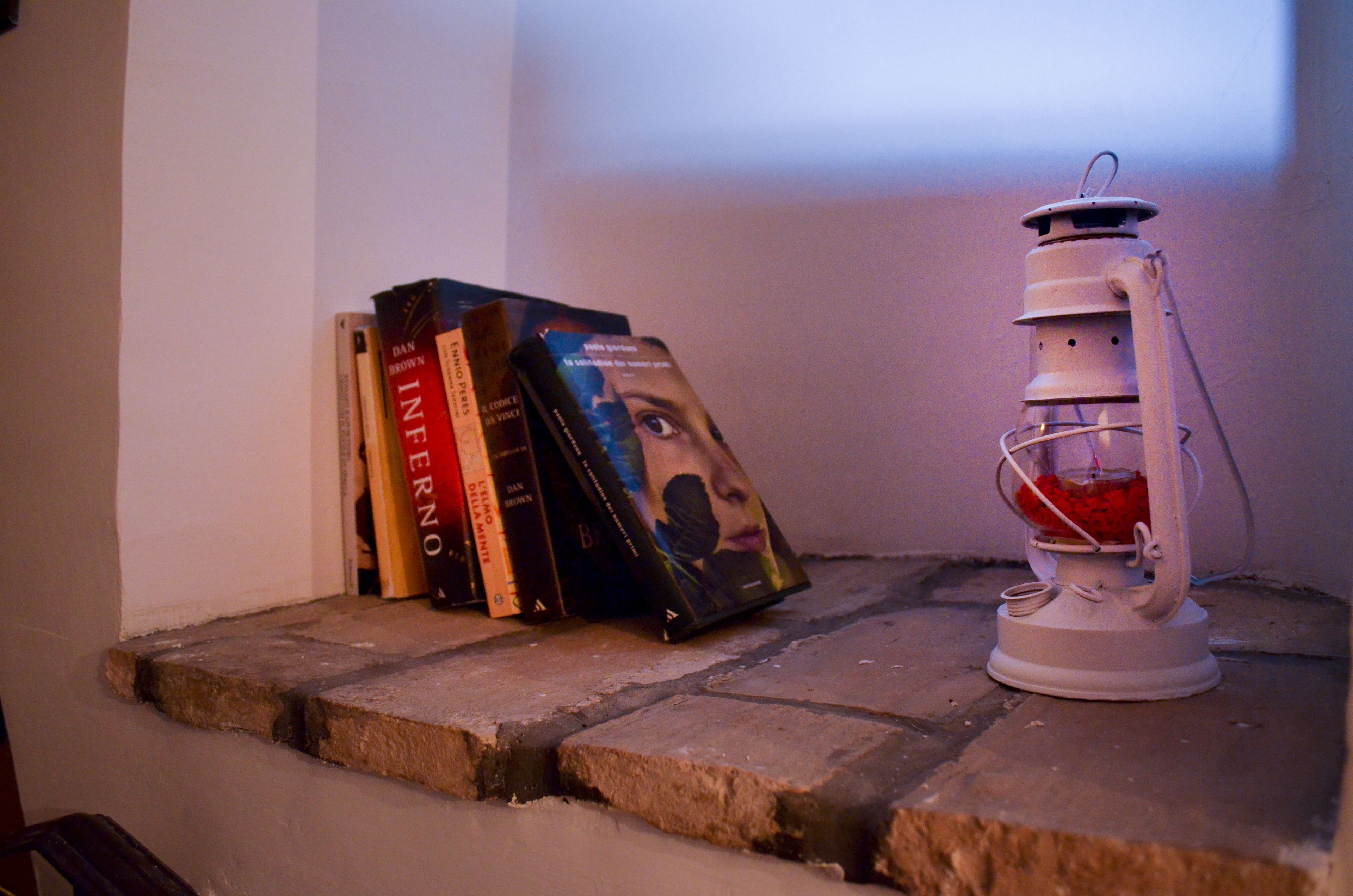 A stack of books on a stone ledge next to a white lantern.