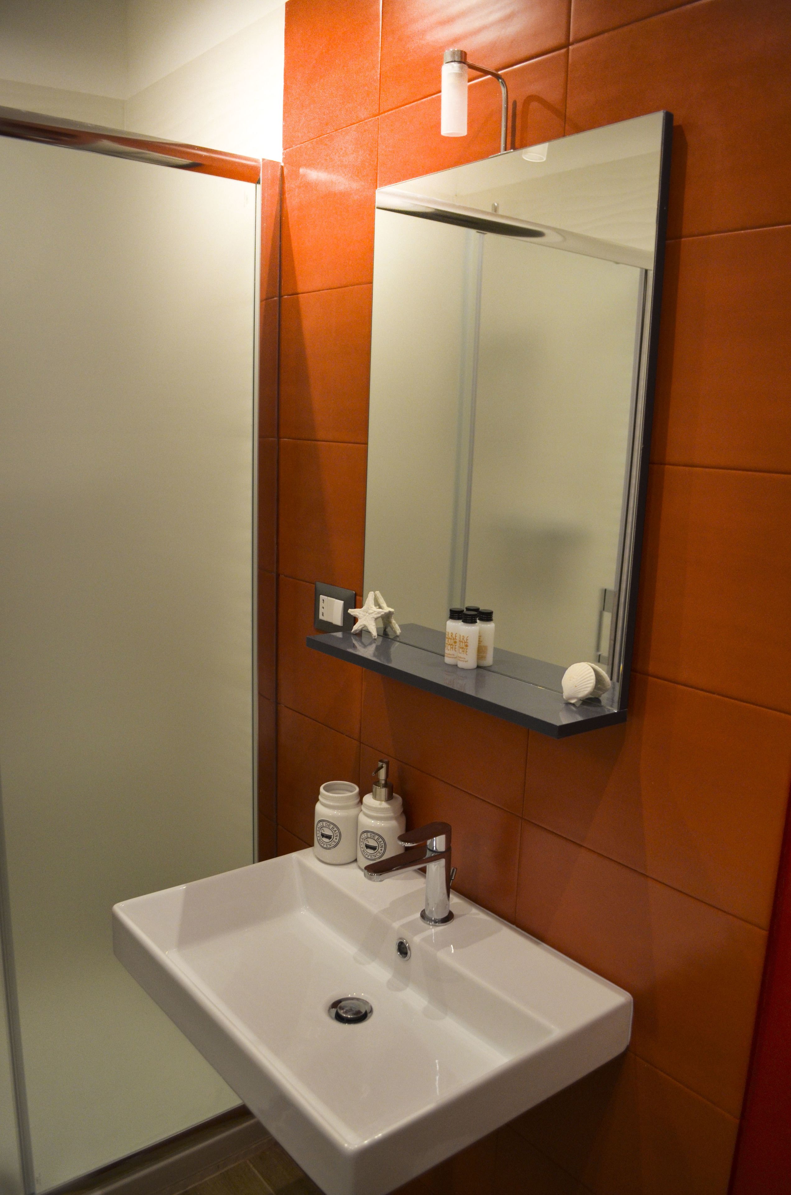 A bathroom with a white sink, a mirror, and orange-tiled walls.