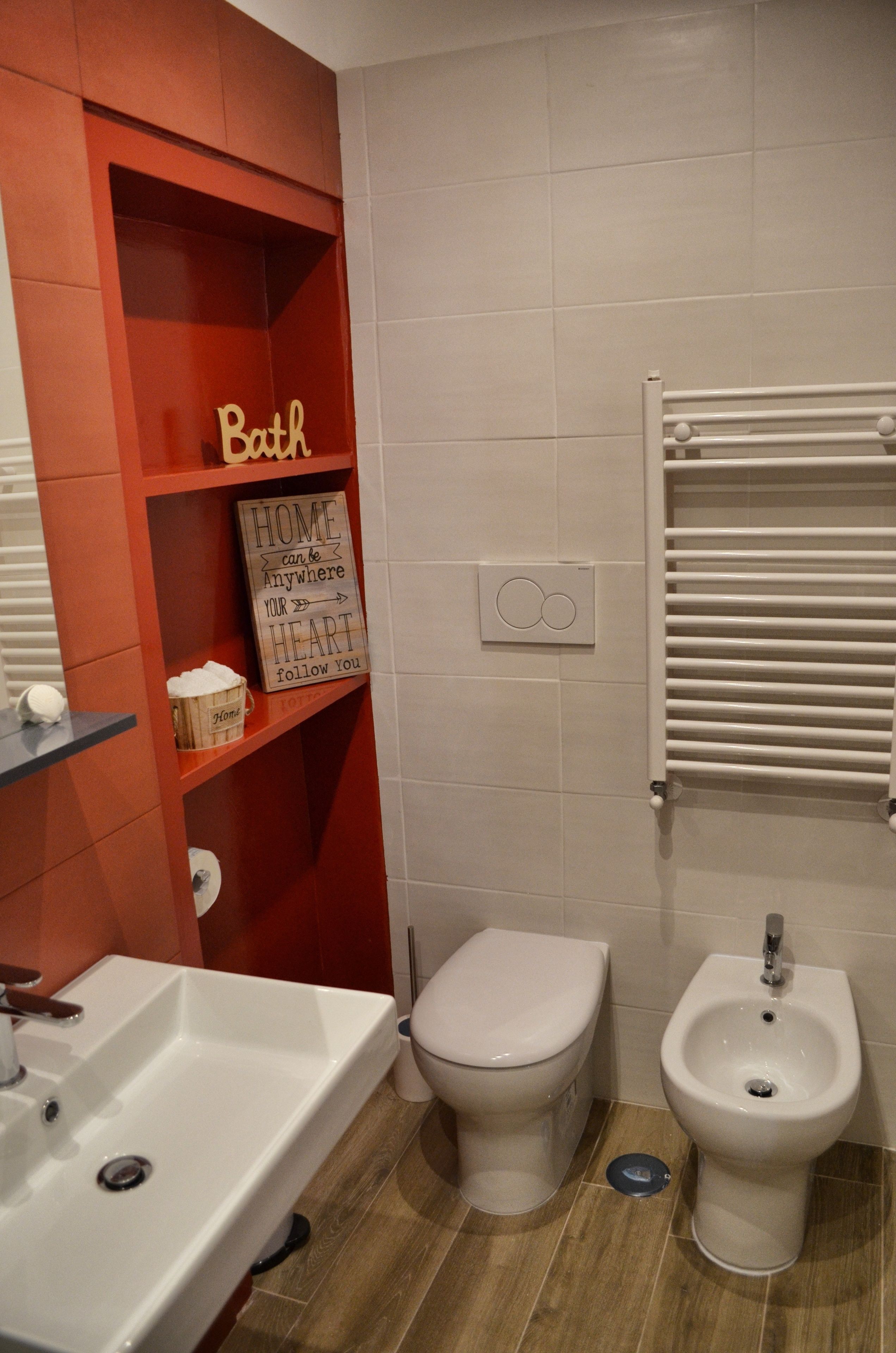 A bathroom with a red shelf, a white sink, a toilet, and a bidet.