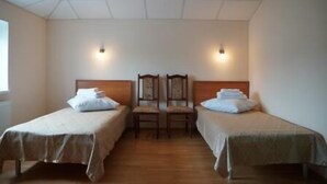 A room with two single beds, wooden headboards, and a wooden chair between them.