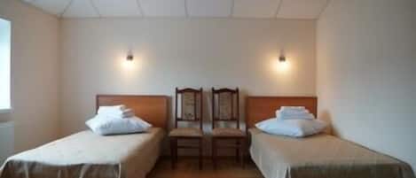 Quarto com duas camas de solteiro, cabeceiras de madeira e uma cadeira de madeira entre elas.