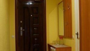 A hallway with wooden flooring, a door, a small sink with a mirror, and a cabinet.
