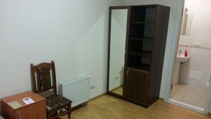 A room with a wooden chair, a small wooden table, a radiator, a wardrobe, and a bathroom with a sink and toilet.