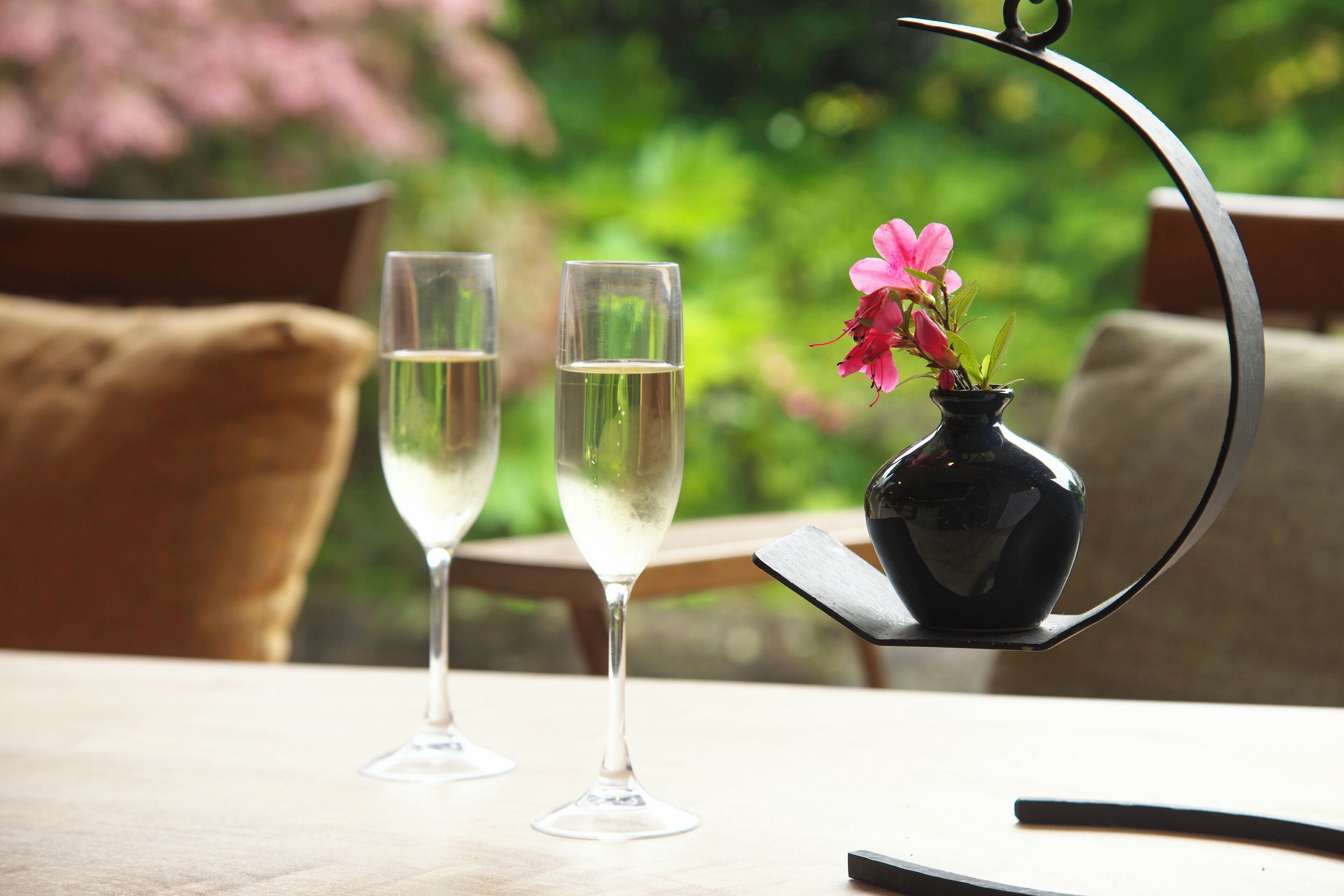 Dos copas de vino blanco sobre una mesa con un florero de flores rosas.