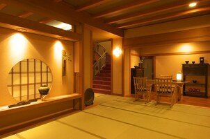 Un interior japonés tradicional con suelo de tatami, una mesa baja con sillas, una escalera y una estantería con objetos decorativos.