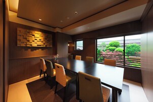 Una sala de conferencias moderna con una gran mesa y sillas, paneles de madera y vistas al exterior con vegetación.