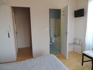 Een slaapkamer met een bed, een kledingkast, een douchegedeelte en een aan de muur bevestigde televisie.