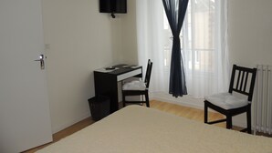 A bedroom with a bed, a desk with a chair, a TV mounted on the wall, and a window with sheer curtains. - Le Gue De Genes (Ambrières-les-Vallées)