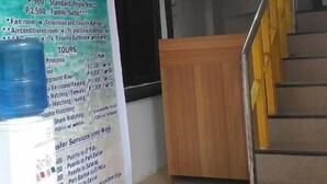 A reception area with a wooden desk and a staircase with yellow railings. A large signboard with room rates and tour information is visible. - Sealor Pension House (Puerto Princesa)