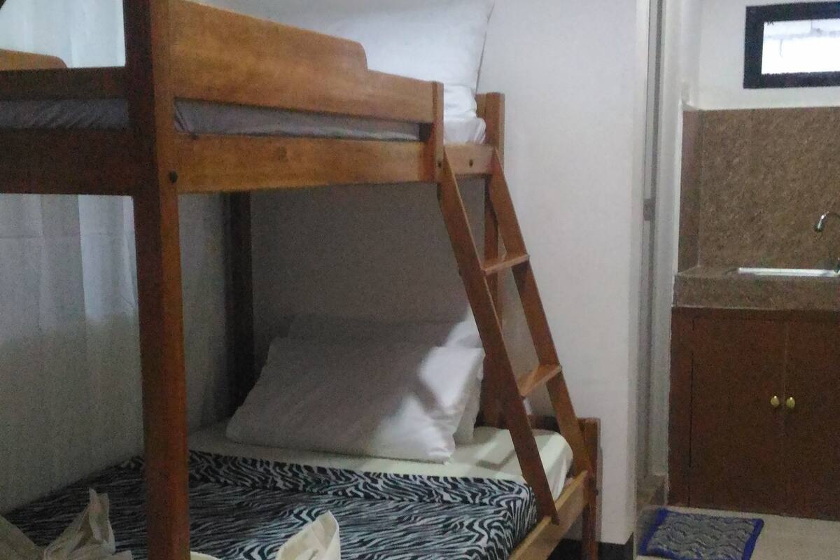 Un lit superposé avec une structure en bois et une literie à motifs, une horloge au mur et une petite armoire avec un miroir.