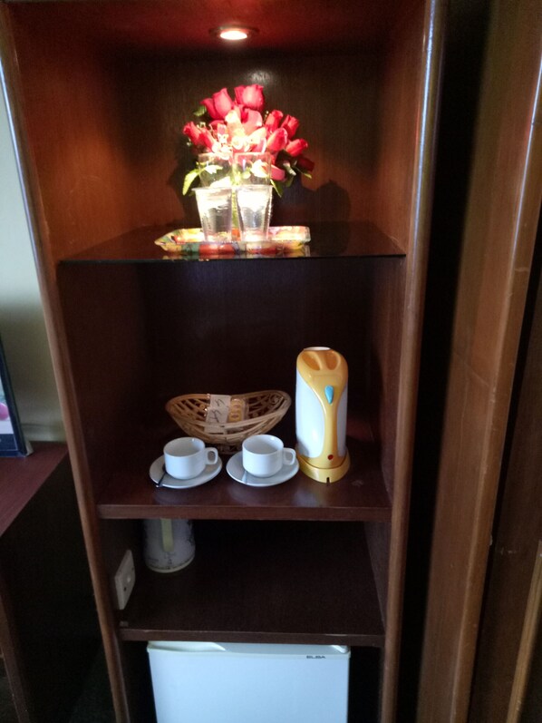 A wooden shelf with a vase of red flowers, two white cups, a wicker basket, and a white appliance. - Hotel Laut Jaya (Tanjung Pinang)