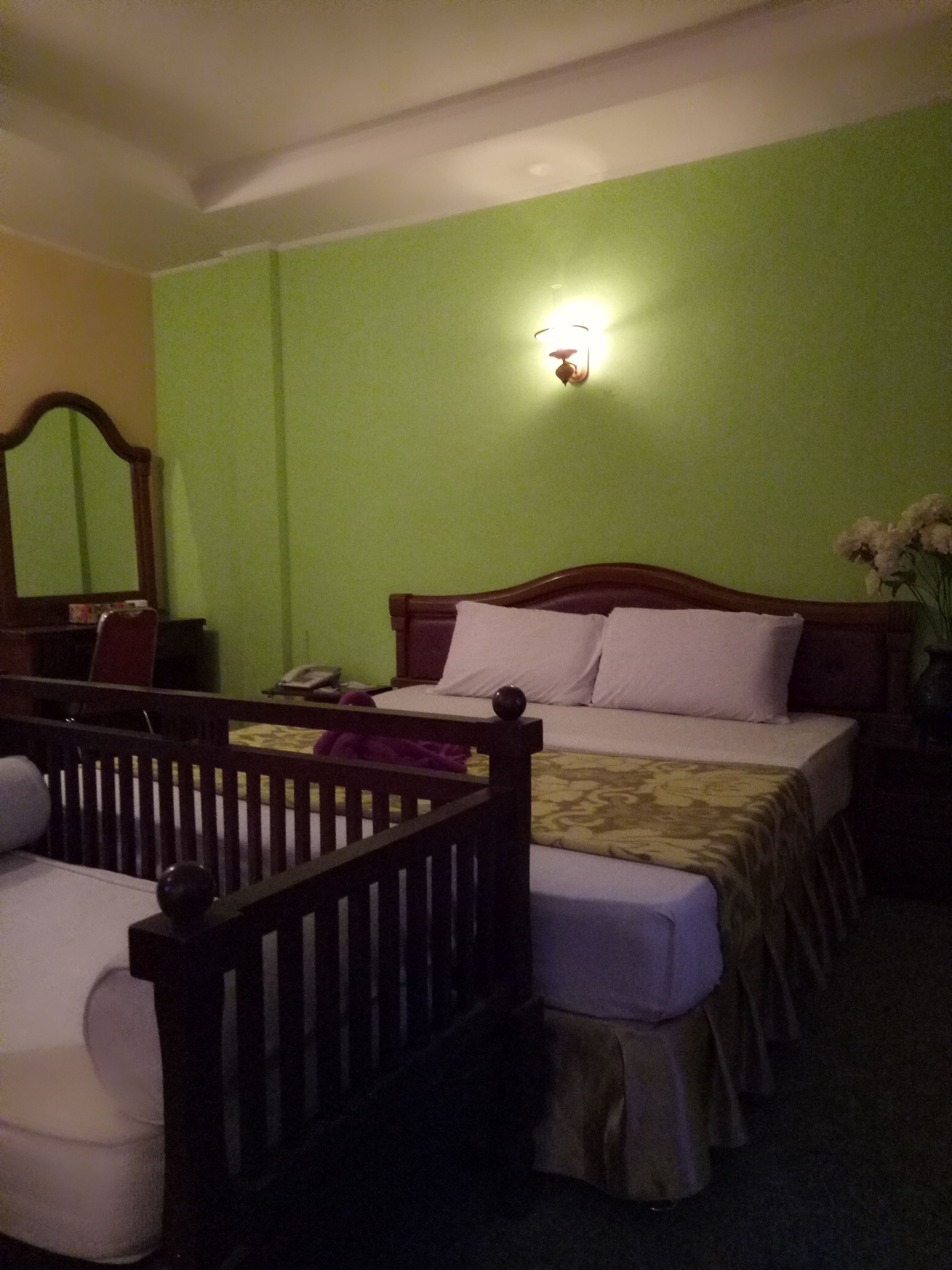 Una habitación con una cama, una cuna de madera, una mesita de noche y un espejo.