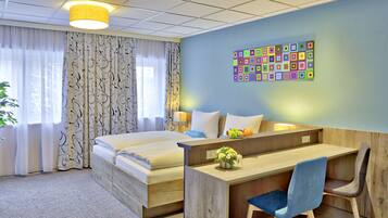 Ein Hotelzimmer mit Bett, Schreibtisch, Stuhl, einer Topfpflanze und einer farbenfrohen Wanddekoration.