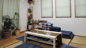 Een woonkamer met tatami matten, een lage tafel, een boekenkast en een televisie op een houten standaard.