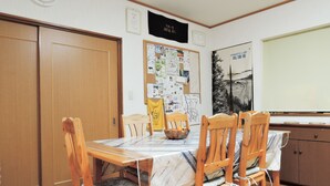Een eetruimte met een houten tafel en stoelen, een prikbord met verschillende documenten, en een klok aan de muur.