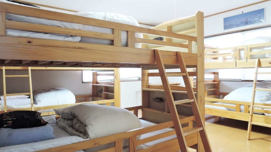 Een slaapkamer met stapelbedden, houten frames, een ladder en een raam.