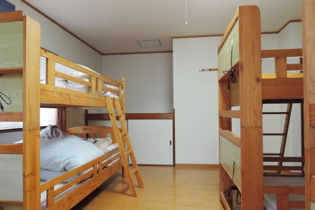 Ein Zimmer mit zwei Etagenbetten, einer Himmelsleiter, einer weißen Tür und Holzdielen.