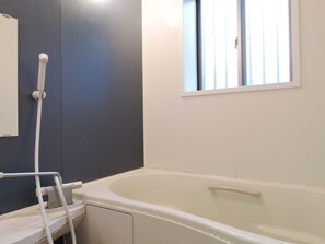 Une salle de bain avec une baignoire, une fenêtre et un flexible de douche.