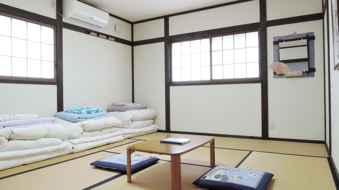 A tatami mat room with a futon bed, a small wooden table, and a window with a view.