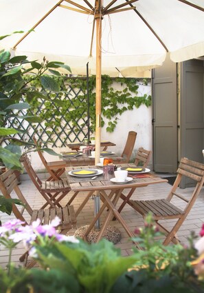 An outdoor patio with a wooden table and chairs, a hanging umbrella, and a lattice wall with climbing plants. - B&B Ponte Manin (Verona)