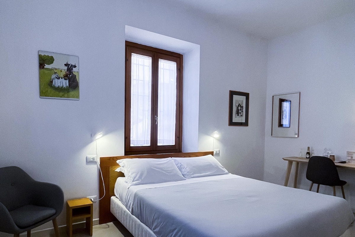 A bedroom with a bed, a chair, a small table, and a window with curtains.