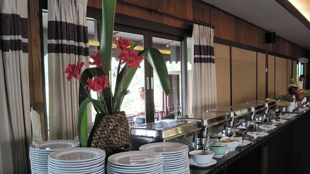 A buffet setup with stacked plates and bowls, a pineapple centerpiece, and a window with curtains. - Coconut Home Resort (Bang Khonthi)