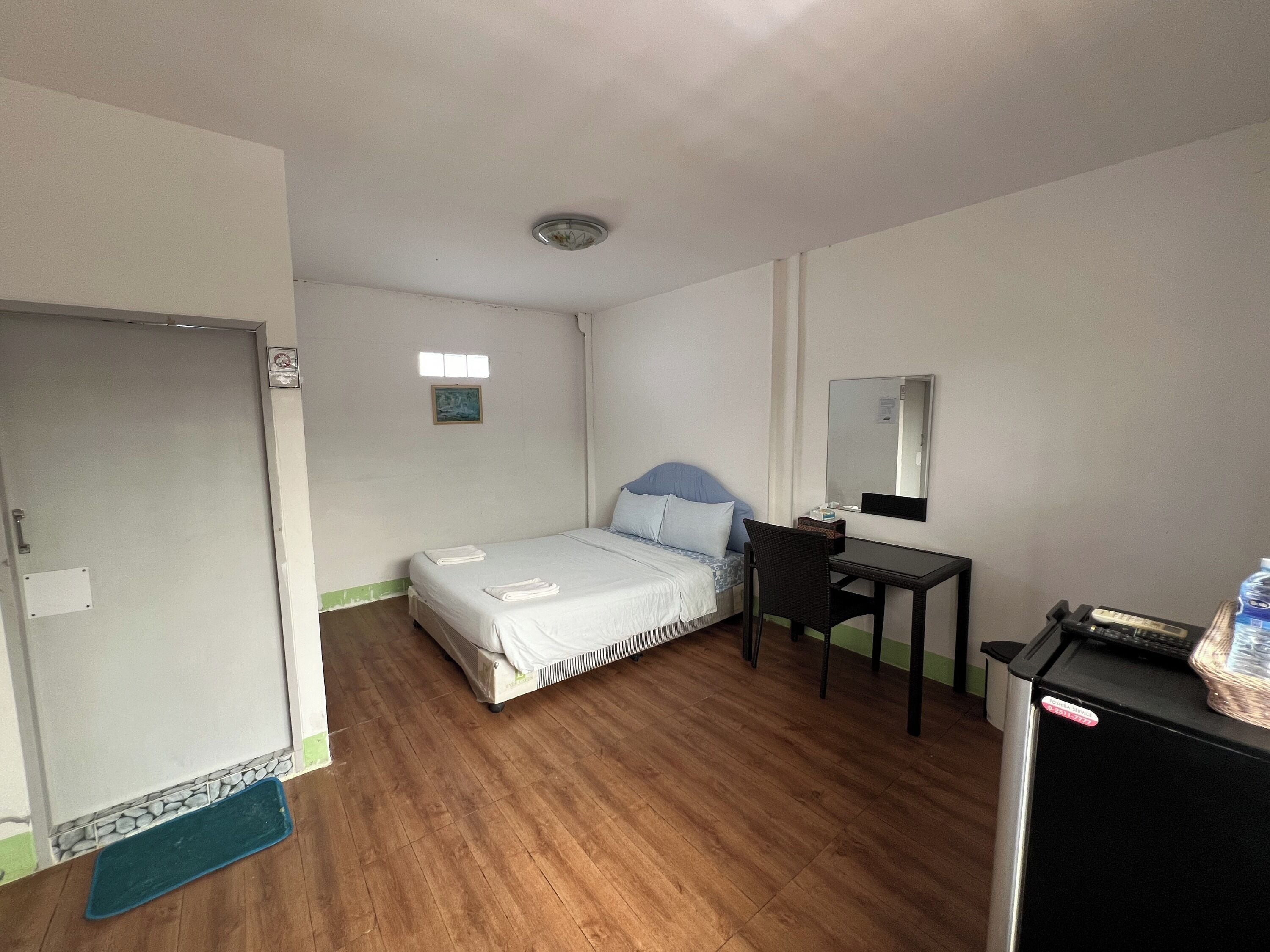 A hotel room with a bed, a desk, a chair, a mirror, and a small refrigerator.
