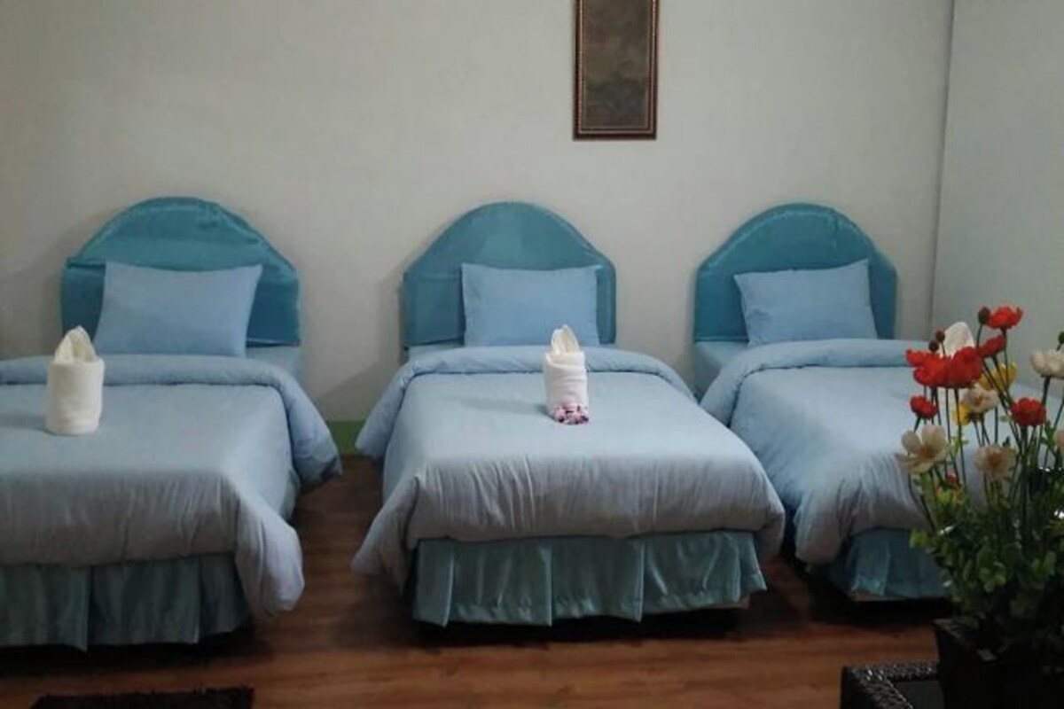 Une chambre avec trois lits, chacun doté d’une tête de lit bleue et d’oreillers assortis.